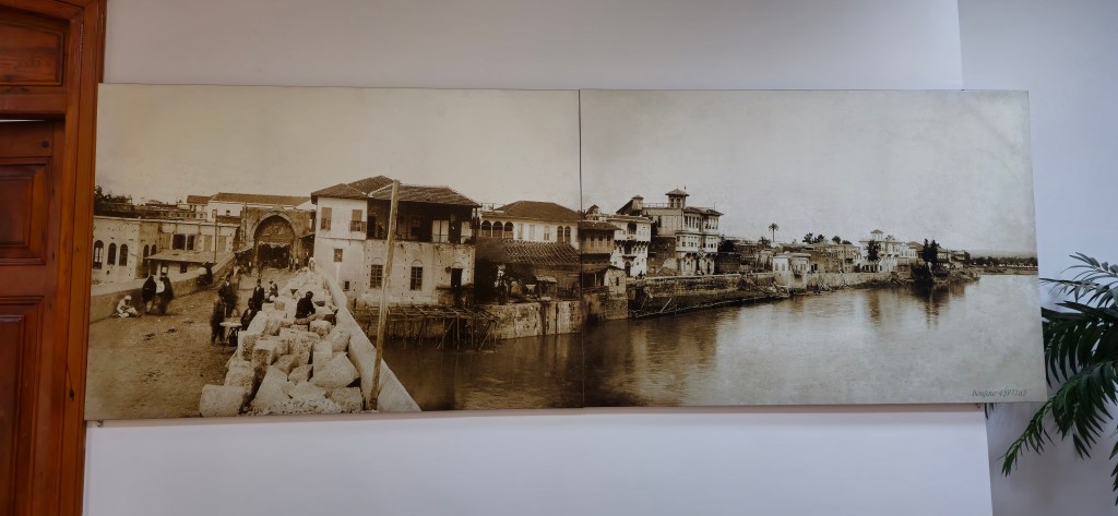 Eski bir kente ait, nehir kenarında yer alan tarihi yapılar ve taş köprü görüntüsü.